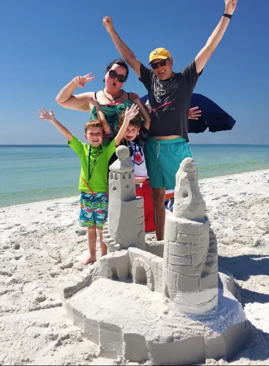 A family celebrates after building an epic sandcastle, thanks to 30A's Beach Sand Sculptures.