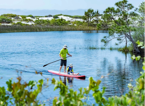 Father and son enjoy paddleboarding across one of 30A's many coastal dune lakes.