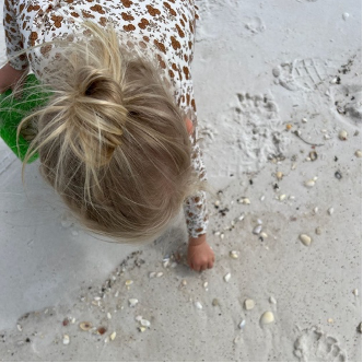A young girl on a 30A beach collects shells.