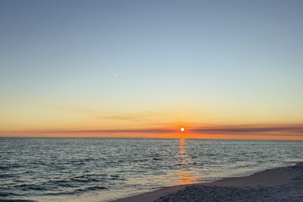 Vibrant orange and pink sunset over 30A beach with calm Gulf waves and silhouetted dunes